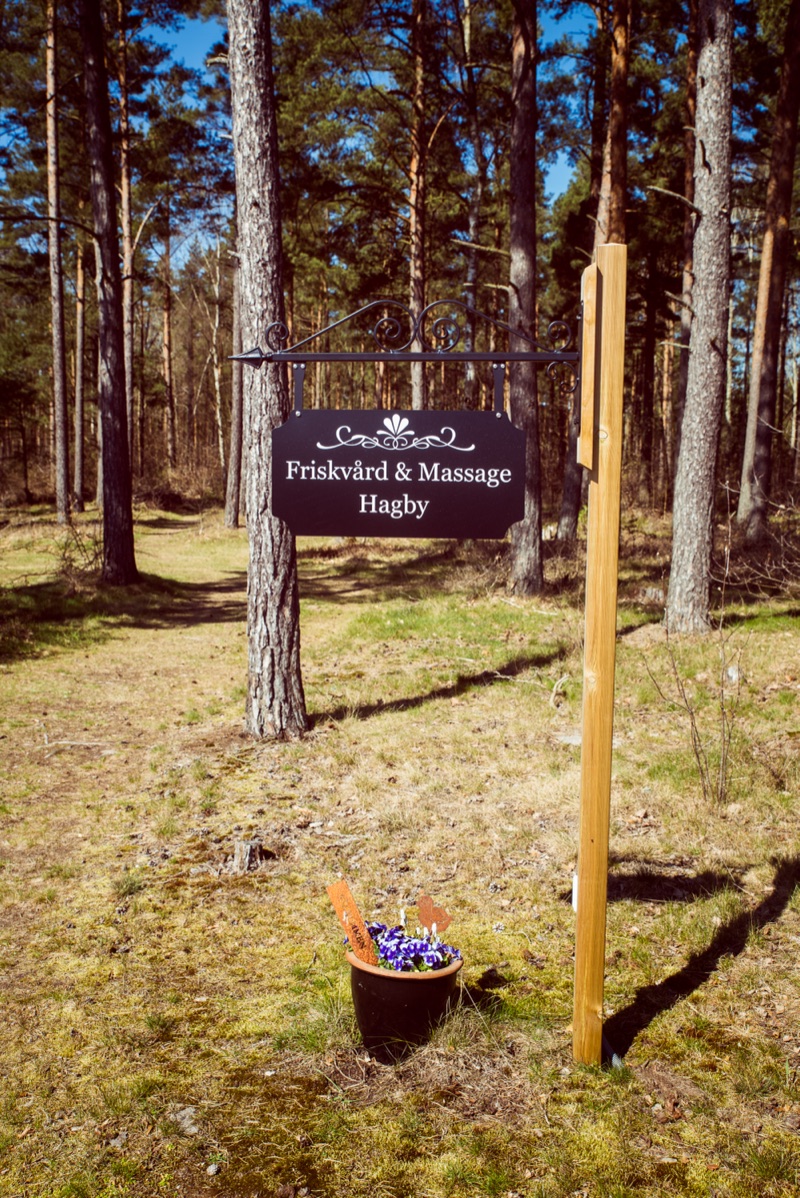 Skylt med texten ”Friskvård & Massage Hagby” på en stolpe i skogen